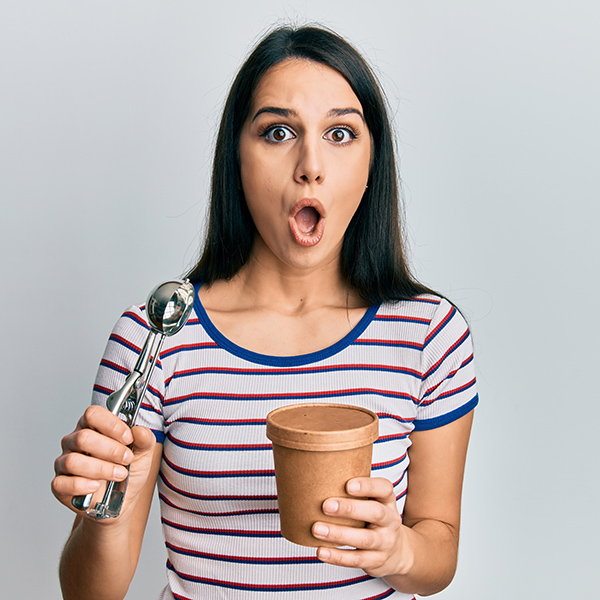 Young hispanic woman holding ice cream afraid and shocked with surprise and amazed expression, fear and excited face.
